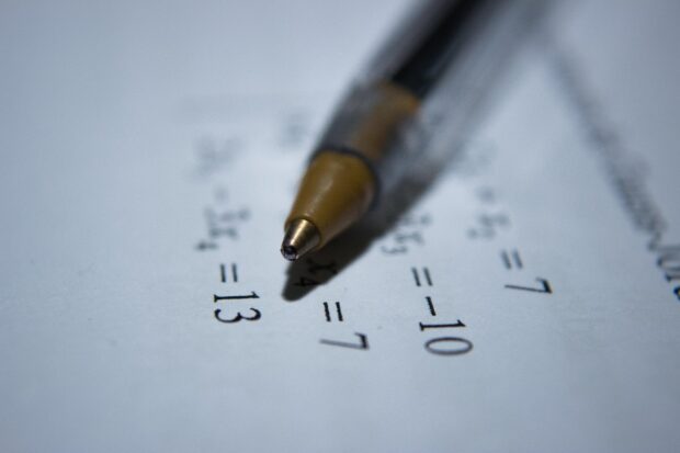 Ball-point pen lying at an angle across a set of equations printed on a sheet of paper.