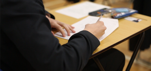 A student at a desk writing on an exam paper.