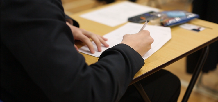 A student at a desk writing on an exam paper.