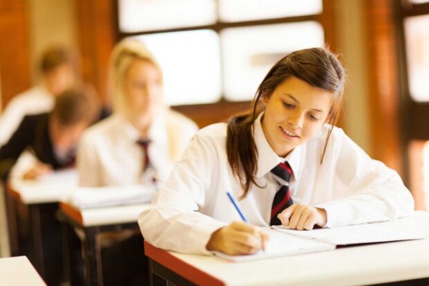 A girl in school uniform taking an exam with other students in the background