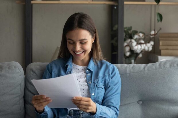 A female student reading her exam results while sitting on a sofa
